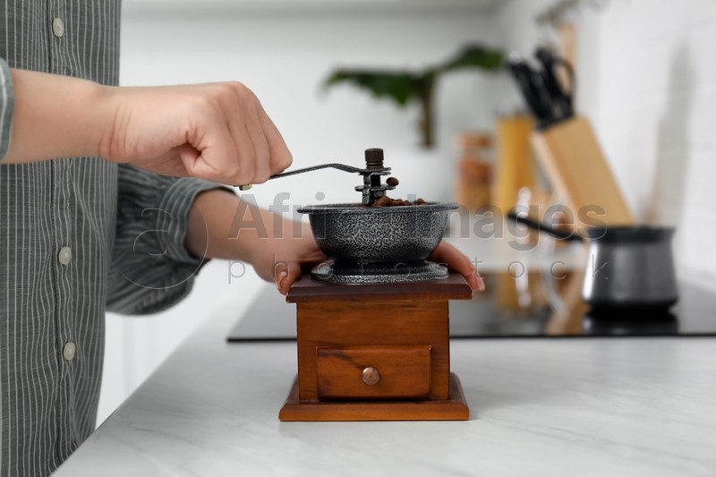 Woman using vintage coffee grinder at countertop indoors, closeup