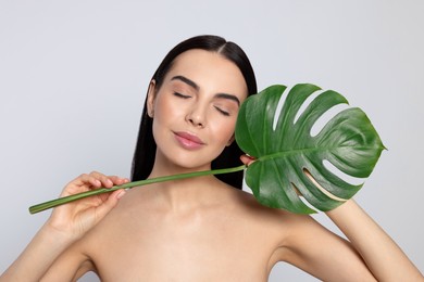 Photo of Woman holding leaf of monstera on light grey background. Spa treatment