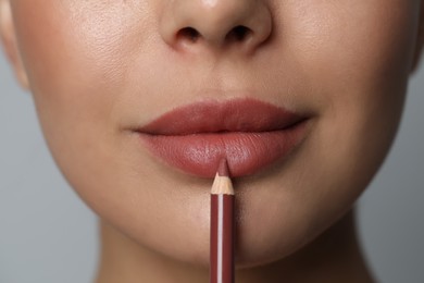 Young woman applying beautiful nude lip pencil on grey background, closeup