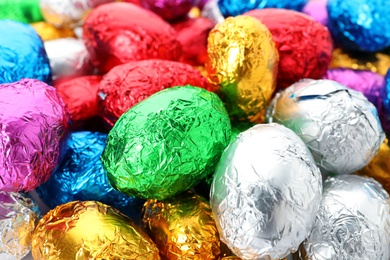 Many chocolate eggs wrapped in bright foil as background, closeup view
