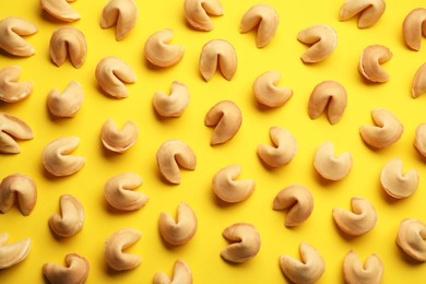 Many tasty fortune cookies with predictions on yellow background, flat lay