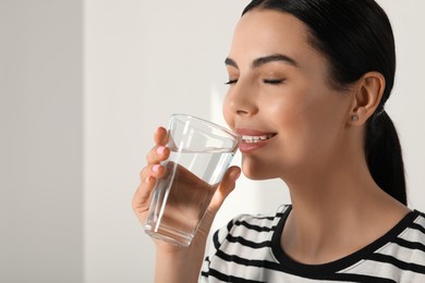 Young woman drinking water indoors, closeup. Refreshing drink. Space for text.