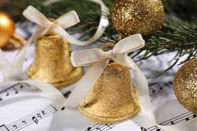 Photo of Golden shiny bells and Christmas decor on music sheets, closeup