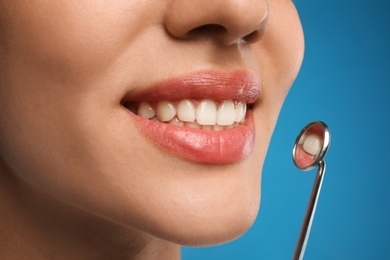 Young woman with mouth mirror on blue background, closeup. Cosmetic dentistry