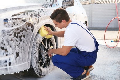 Worker cleaning automobile with sponge at car wash