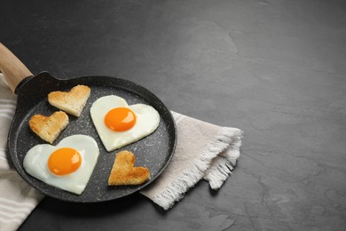 Heart shaped fried eggs and toasts in frying pan on grey table, space for text