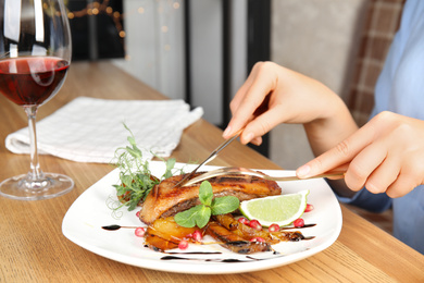 Photo of Woman eating delicious grilled duck breast served at wooden table, closeup