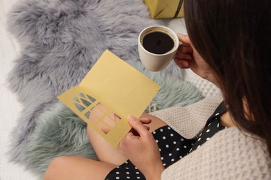 Photo of Young woman with greeting card and hot drink sitting indoors, closeup