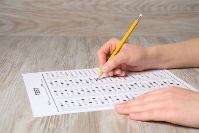Photo of Student filling answer sheet at wooden table, closeup. Passing exam