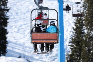 Photo of People using chairlift at mountain ski resort, back view. Winter vacation
