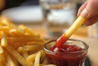 Woman dipping French fries into red sauce in cafe, closeup