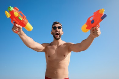 Man with water guns having fun against blue sky, low angle view
