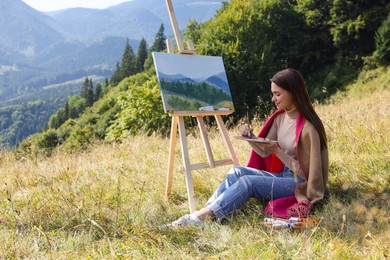 Photo of Young woman drawing on easel in mountains