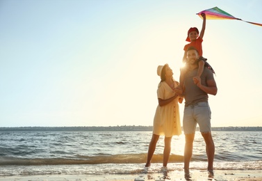 Happy parents and their child playing with kite on beach near sea. Spending time in nature
