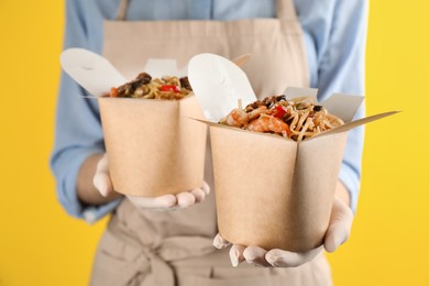 Chef holding boxes of wok noodles with seafood on yellow background, closeup