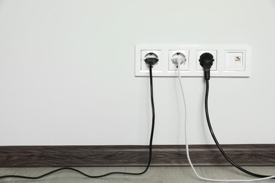 Power sockets with inserted plugs on white wall indoors, space for text. Electrical supply