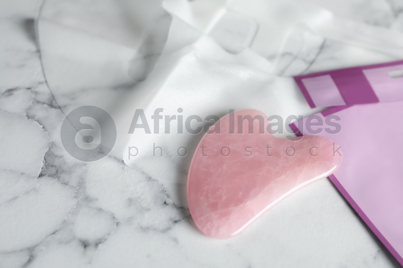 Photo of Rose quartz gua sha tool and facial mask on white marble table