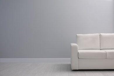Comfortable white sofa near light wall indoors, space for text. Simple interior