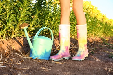 Photo of Young woman in rubber boots with watering can at lily field, closeup. Flower gardening