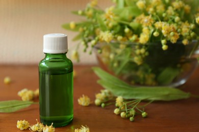 Bottle of essential oil and linden blossoms on wooden table, closeup. Space for text