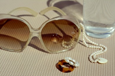 Stylish sunglasses, glass of water and jewelry on grey surface, closeup