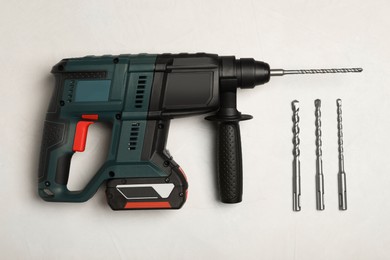 Modern electric power drill and different bits on white table, flat lay
