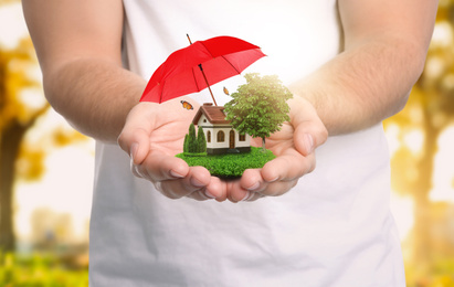 Insurance concept - umbrella demonstrating protection. Man holding house model with green lawn, closeup