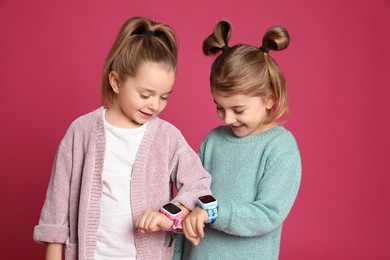 Little girls with smart watches on pink background