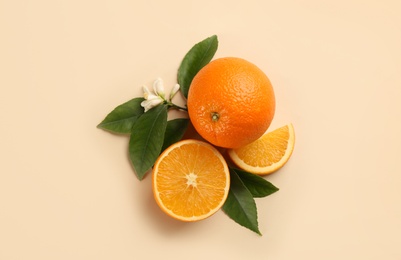 Fresh ripe oranges with green leaves and flower on beige background, flat lay
