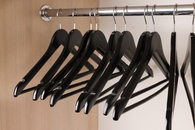 Photo of Set of black clothes hangers on wardrobe rail, closeup
