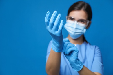 Doctor in protective mask and medical gloves against blue background, focus on hands. Space for text