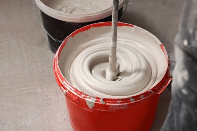 Mixing putty with electric mixer in red bucket indoors