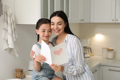 Photo of Little daughter congratulating her mom in kitchen at home. Happy Mother's Day