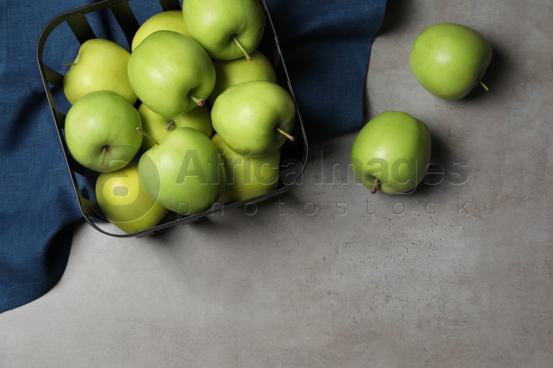 Black metal container full of apples and napkin on grey table, flat lay. Space for text