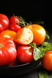Many different ripe tomatoes with leaves on black table, closeup