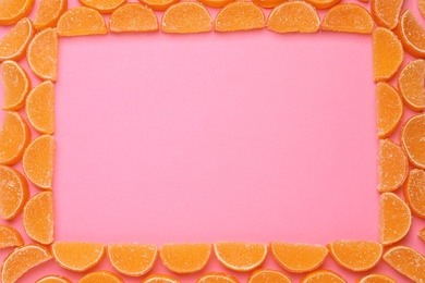 Frame made with orange marmalade candies on pink background, flat lay