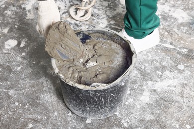 Photo of Worker with trowel mixing concrete in bucket indoors, closeup