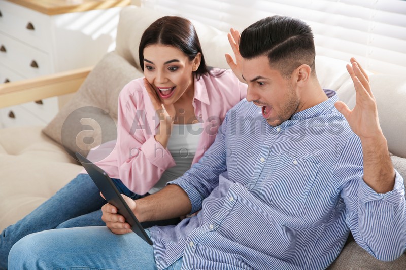 Emotional couple participating in online auction using tablet at home