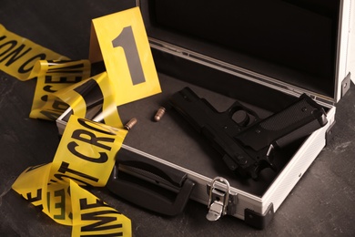 Open case with gun, bullets and crime scene marker on black table, closeup