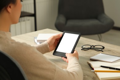 Young woman using e-book reader at wooden table indoors, closeup