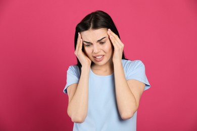 Woman suffering from migraine on pink background