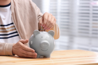 Man putting coin into piggy bank at wooden table, closeup. Space for text