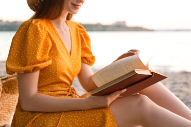 Young woman reading book on sandy beach near sea, closeup