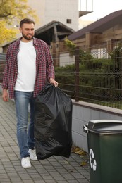 Man carrying garbage bag to recycling bin outdoors