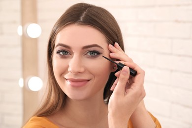 Photo of Beautiful young woman applying black eyeliner indoors