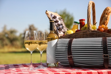 Picnic basket with wine, snacks and mat on table in park