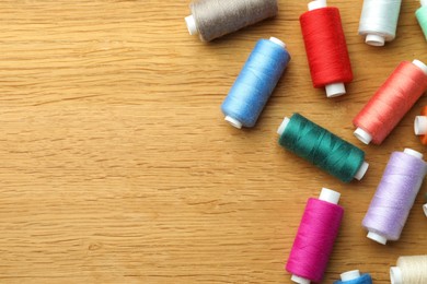 Many colorful sewing threads on wooden table, flat lay. Space for text
