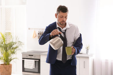 Sleepy man pouring coffee into cup at home in morning