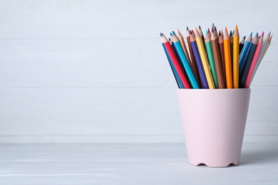 Colorful pencils in cup on white wooden table. Space for text