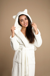 Beautiful young woman in bathrobe with funny hood on brown background